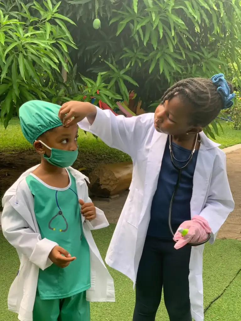 Two children dressed as doctors, one checking the other with a stethoscope in the school garden