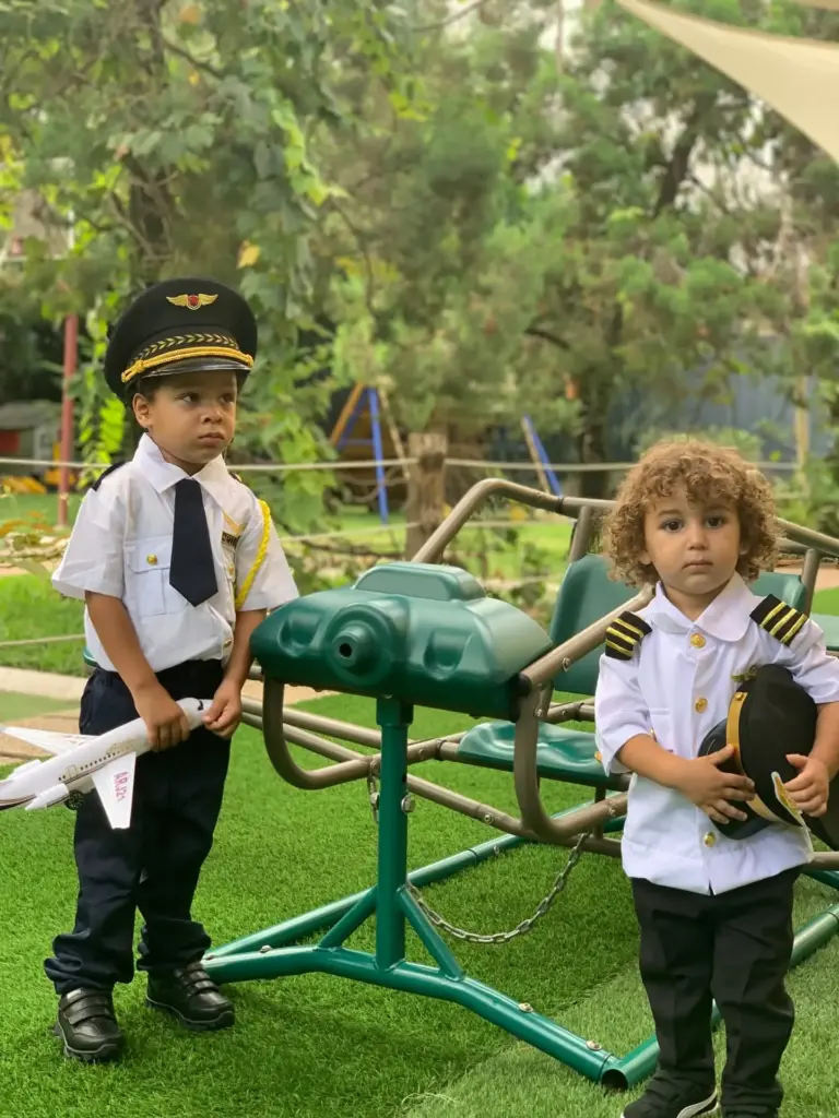 Two boys dressed as airline pilots, one holding a model plane, on the playground lawn
