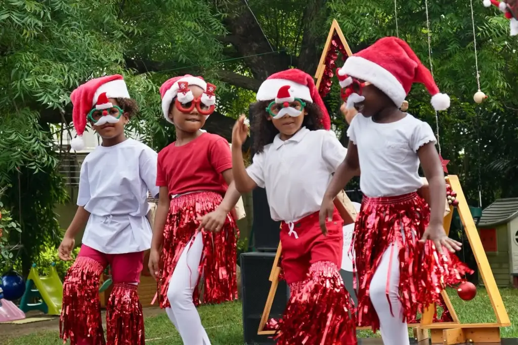 Children in Santa hats and red tinsel performing a dance at the Christmas show