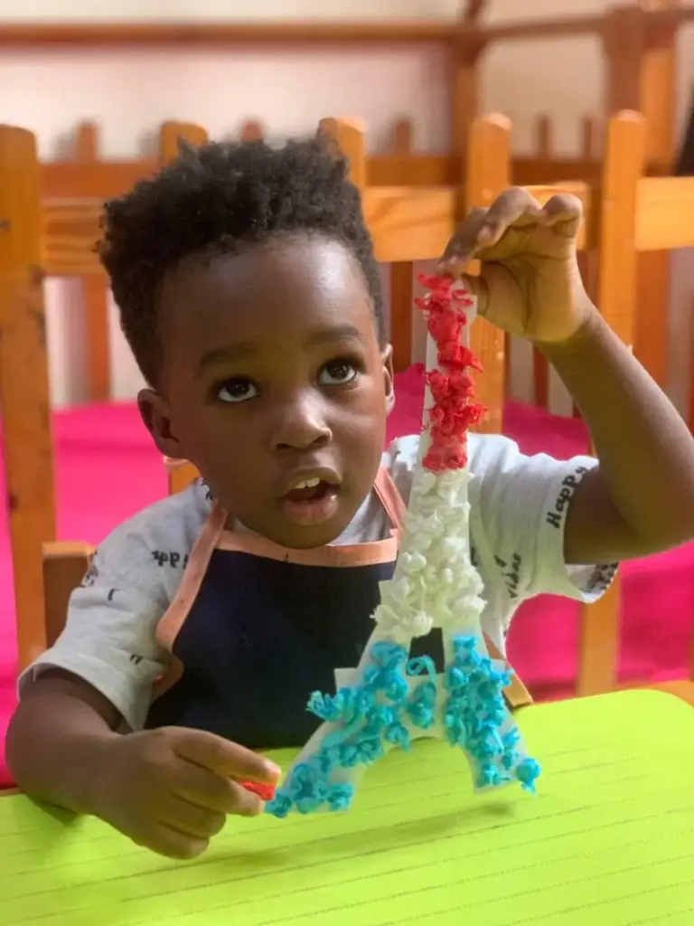 Boy holding up a red, white and blue Eiffel Tower he made in class