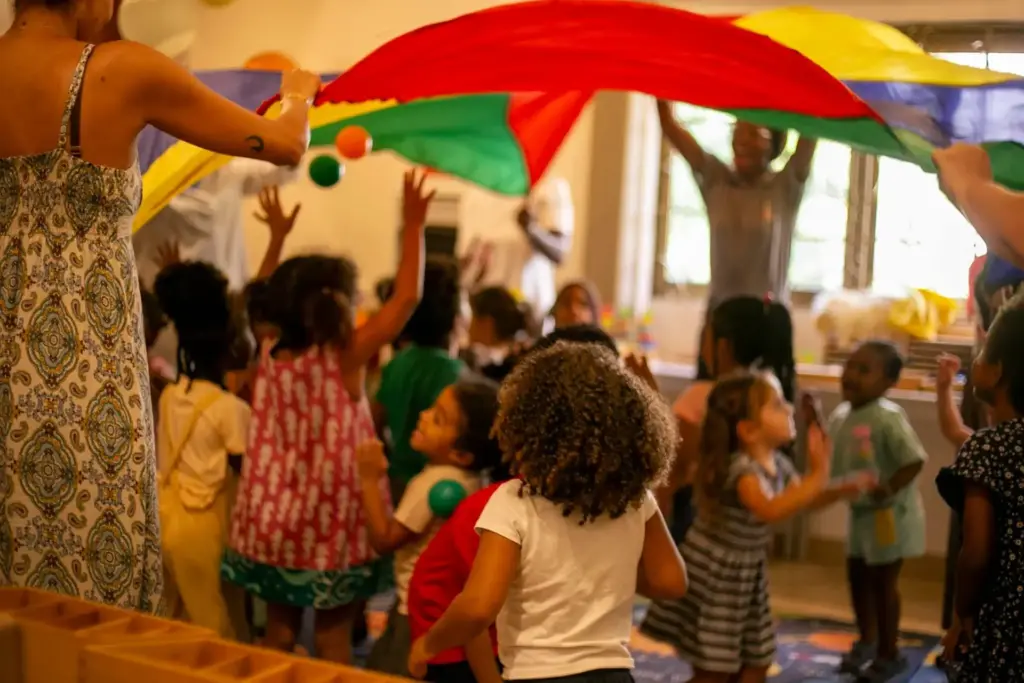 Children and adults lifting a rainbow play parachute in the classroom