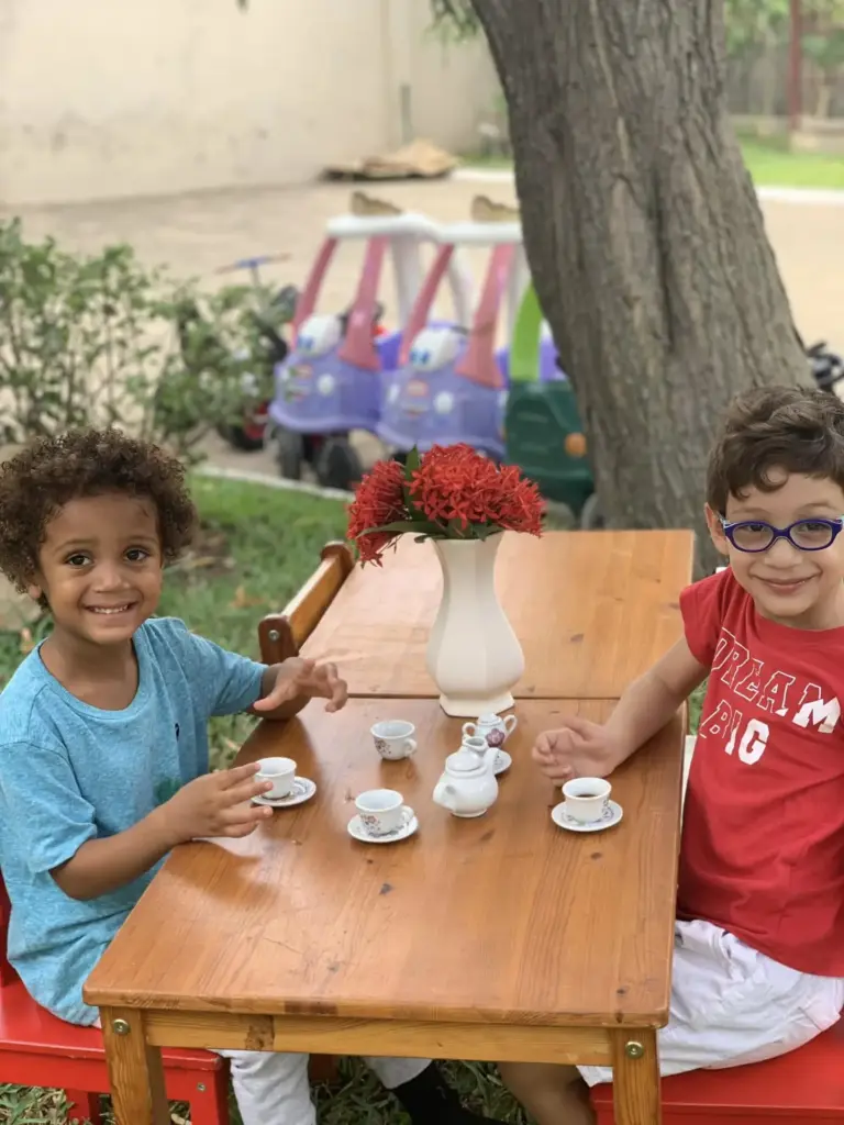 Two smiling boys having a tea party with a china tea set at a garden table