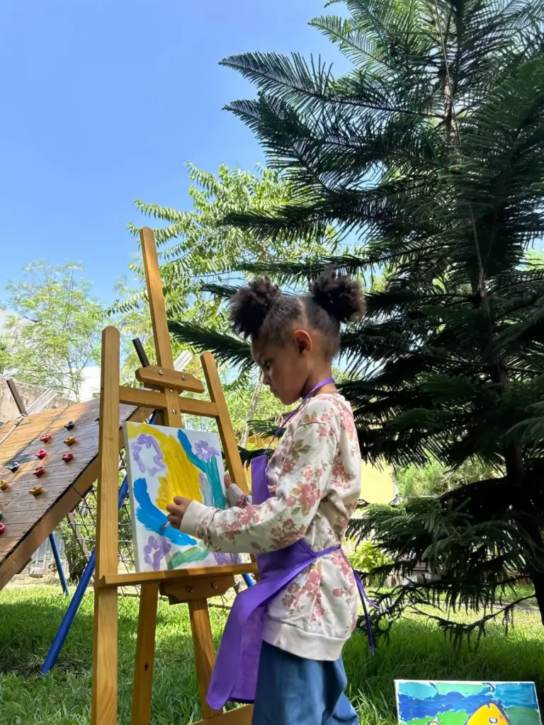 Girl painting at an easel outdoors beside the pine trees