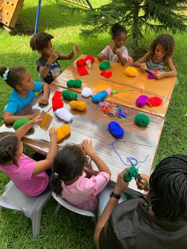 Children around an outdoor table weaving with balls of colourful yarn
